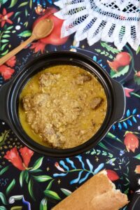 A bowl of Adjarian yakhni – Georgian beef stew with walnuts and spices, served with bread on a rustic table
