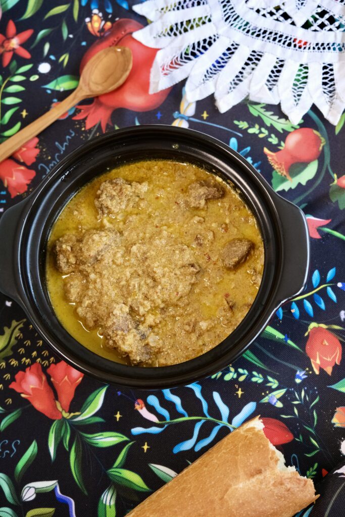A bowl of Adjarian yakhni – Georgian beef stew with walnuts and spices, served with bread on a rustic table