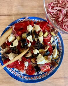 Crispy eggplant salad with cherry tomatoes, sumac onions, rice noodles, and feta, served in a white bowl with fresh herbs.